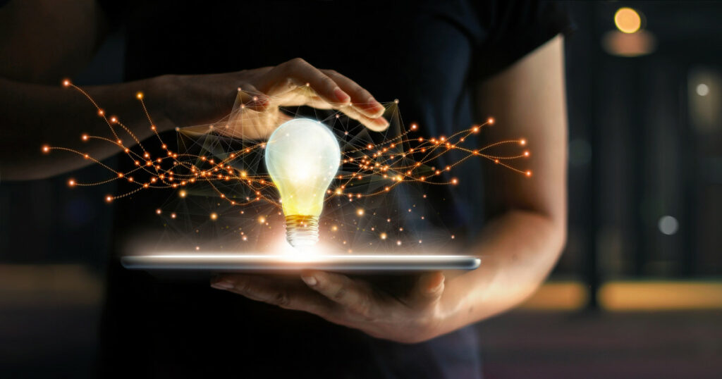 An image illustrating innovative marketing strategies with a female's hand hovering over a lightbulb suspended over a laptop