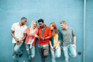 A diverse group of Generation Z standing against a wall using digital technology